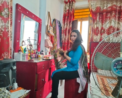 Photo of a transgender person in Pakistan, seated at a vanity with a fan in the foreground.